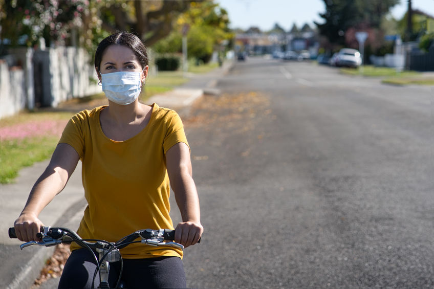 Young hispanic woman riding her bicycle and wearing a face mask against covid-19