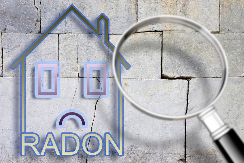 The danger of radon gas in our homes – concept image with an outline of a small house with radon text against a cracked stone wall with a magnifying glass